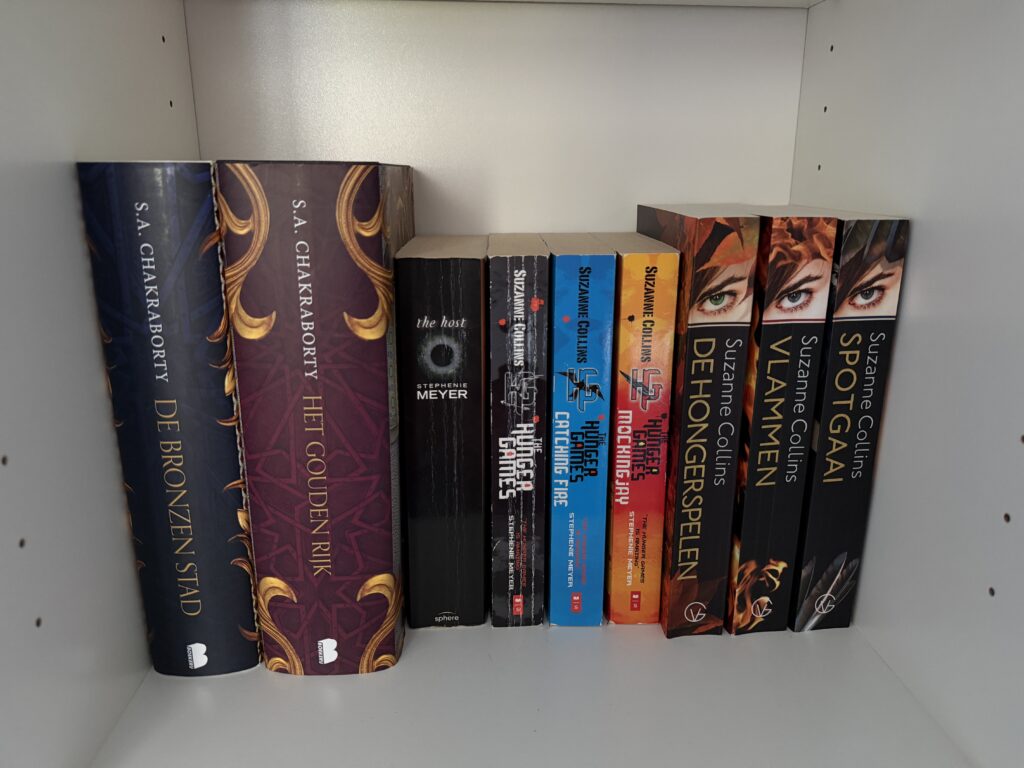 Boekenplank met fysieke boeken, waaronder de Hunger Games-serie en De Bronzen Stad van S.A. Chakraborty